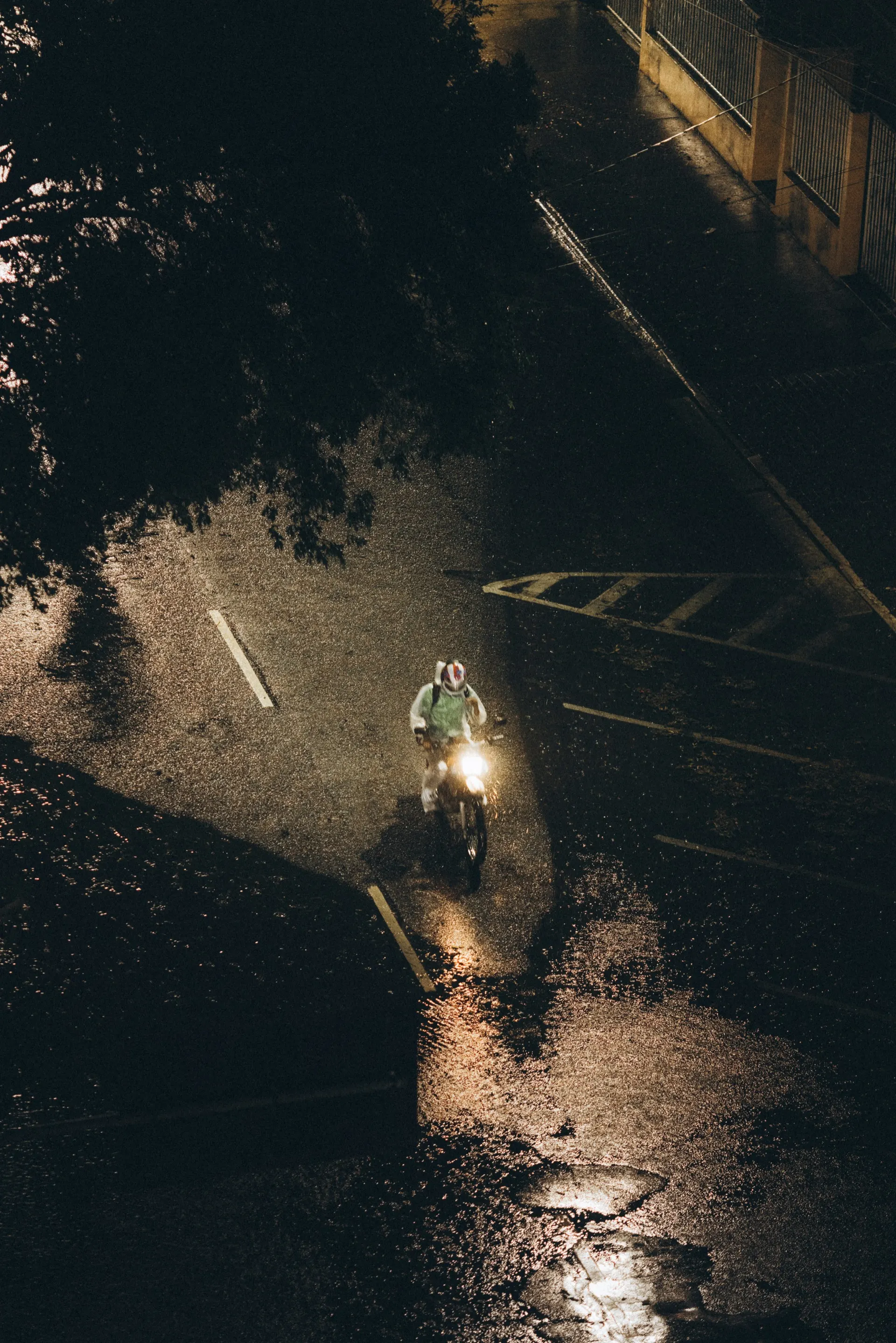 A lone rider on a matte black motorcycle crossing a rain-slicked city street at night