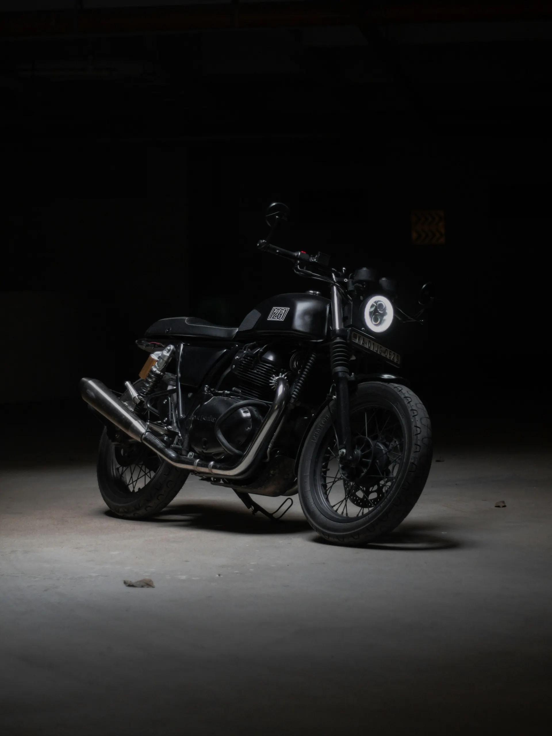 A matte black motorcycle isolated under a single spotlight in a dark concrete garage